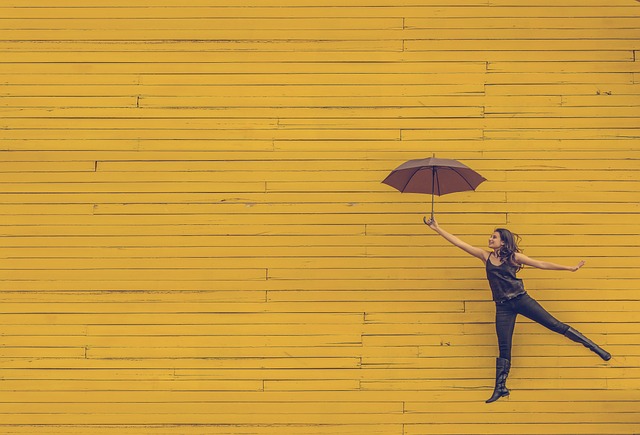Woman umbrella flying again yellow wood wall - by pexels from pixabay