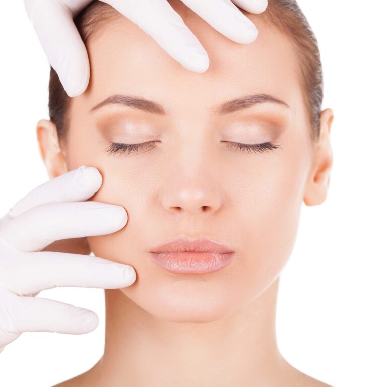 Preparation before facial surgery. Beautiful young woman keeping eyes closed while doctor in medical gloves examining her face isolated on white